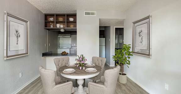 A dining room with a table set for two and a potted plant.