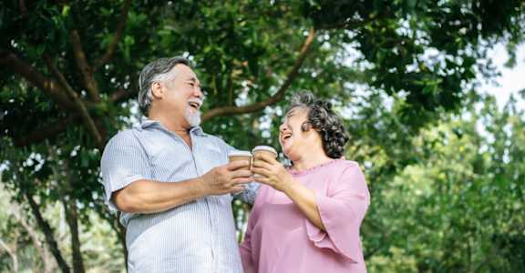 a man and a woman standing in front of a tree holding cups of coffee