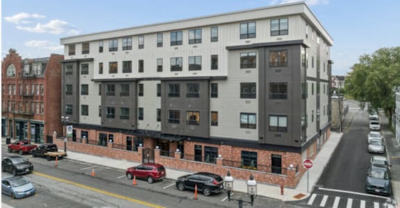 A street view of a multi-story building with cars parked in front.