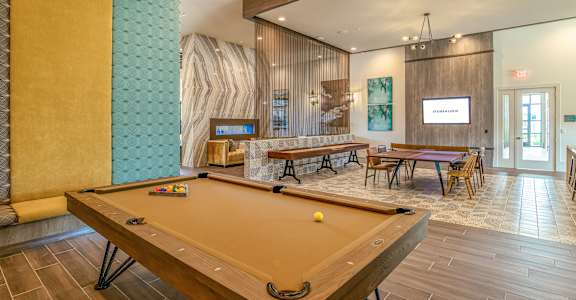 A pool table is in the middle of a room with a wooden floor and a wall with a green pattern at Stone Loch Apartments, Texas