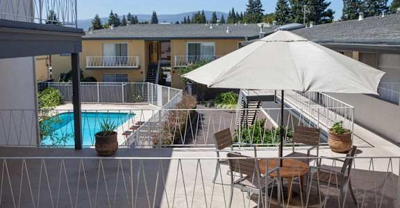 A patio with a table, chairs, and an umbrella overlooking a pool.