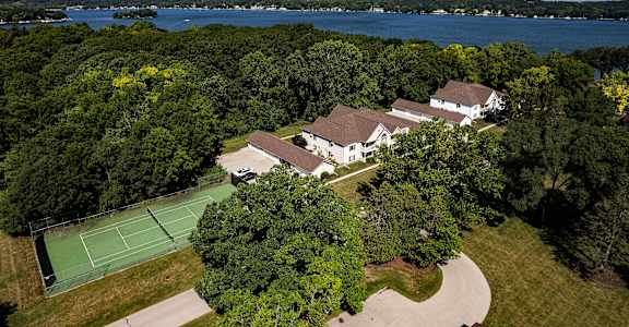 a mansion with a tennis court and a lake in the background