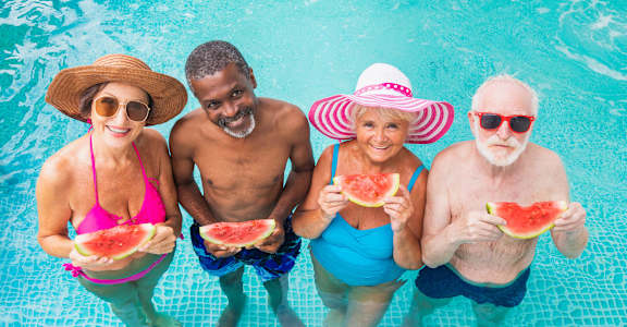 people in a pool eating watermelon and wearing hats and sunglasses at 55+ FountainGlen Seacliff, Huntington Beach, CA