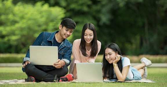three friends sitting outside using laptops