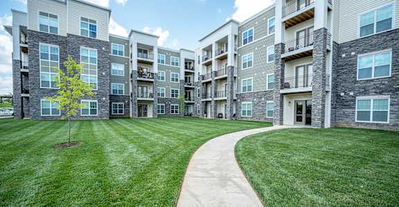 A tree is planted in a grassy area in front of apartment buildings at Waterstone at Hamburg Apartments, Kentucky, 40509