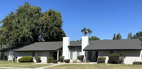 a white house with a gray roof and a tree