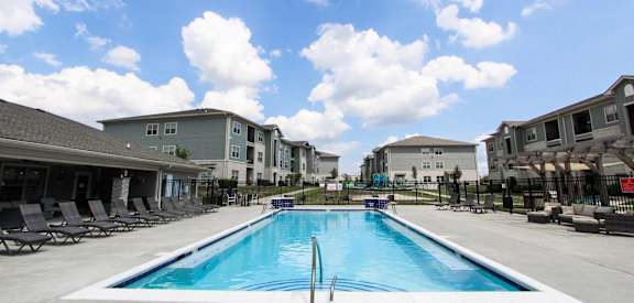 A swimming pool in front of a building with lounge chairs around it.
