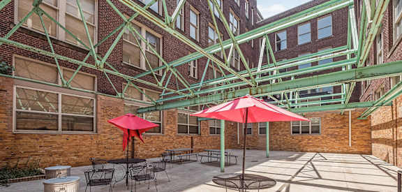 a patio with tables and umbrellas in front of a brick building