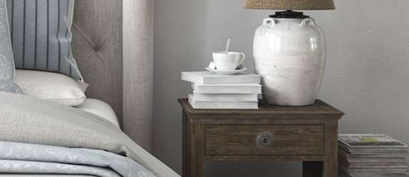 a nightstand with a lamp and books on it next to a bed