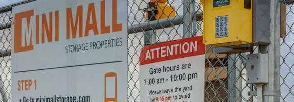 A sign for the Mini Mall Storage Properties is displayed on a fence.