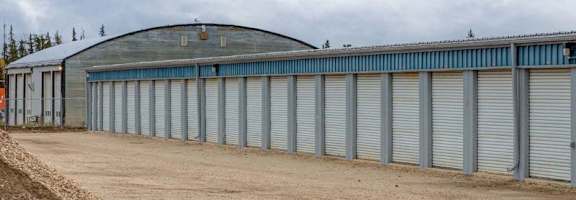 A long row of grey storage units with a dirt road in front.
