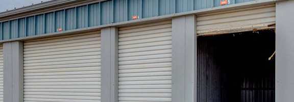 A storage unit with a closed grey door and an open door revealing a dark interior.