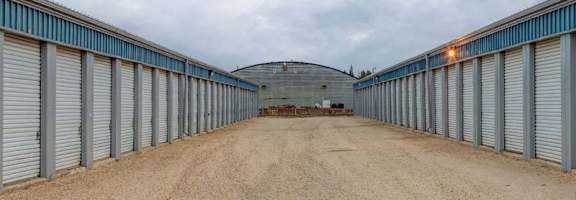 A long, narrow storage facility with a dirt road leading to a circular building in the middle.