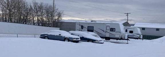 A car is parked in the snow next to a trailer.