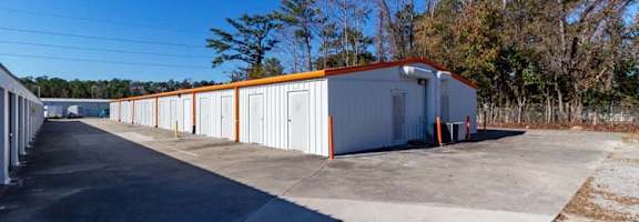 A long white building with orange trim is situated in a parking lot.