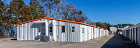 A long building with orange trim is surrounded by a parking lot.