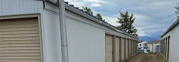A long row of storage units with closed doors and a dirt path down the center.