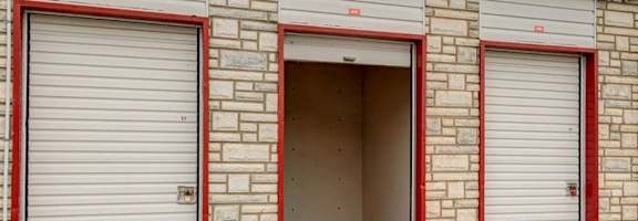 A building with red trim and a red roof has three garage doors.