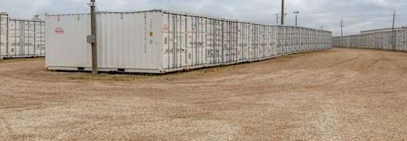 A row of white shipping containers are lined up in a field.
