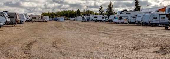a row of rvs parked in a dirt lot with clouds in the sky