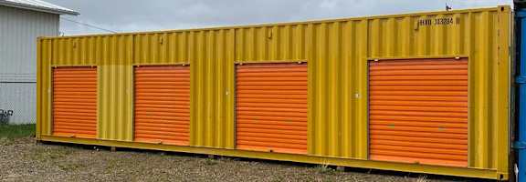 A yellow container with orange doors is parked in a gravel lot.