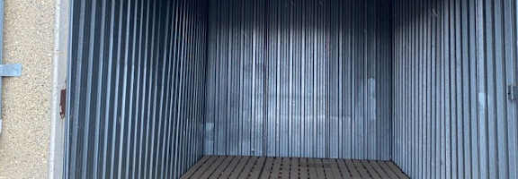 The image shows the interior of a storage unit with a wooden floor and metal walls.