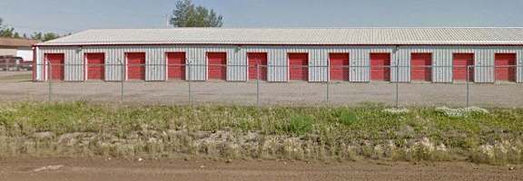 A long building with red doors is surrounded by a fence.