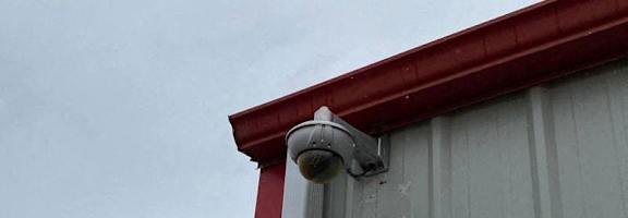 A grey building with a red trim and a security camera mounted on it.