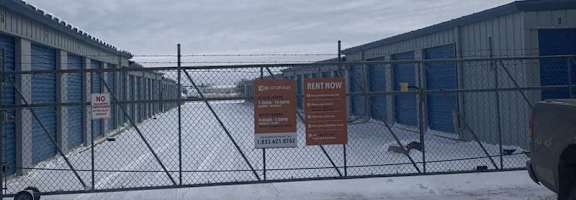 A snowy scene with a fence and a sign that says "NO PARKING ANY TIME".