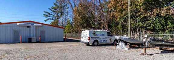 A white van is parked in front of a white building with a boat on the ground.