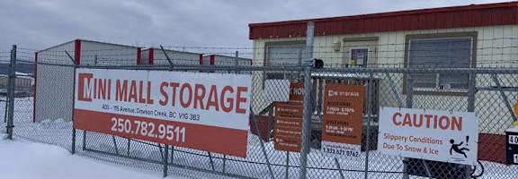 A storage facility is covered in snow and has a caution sign for slippery conditions.