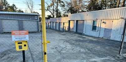 a parking lot in front of a building with a fence and a yellow parking meter