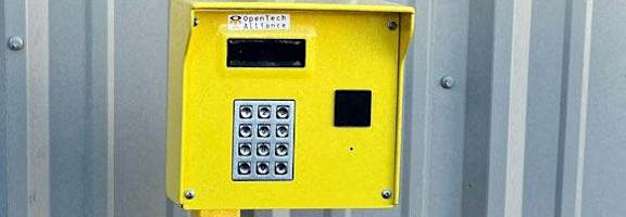 A yellow box with a keypad and a small screen is mounted on a metal pole.