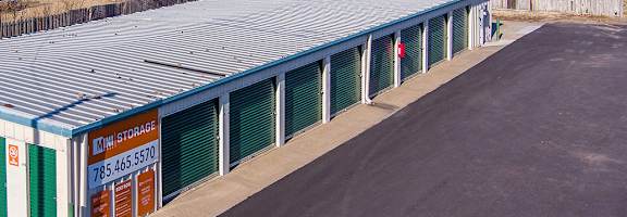 A mini storage facility with a blue roof and green doors.