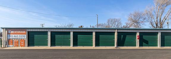 A storage facility with green doors and an orange sign on the side.
