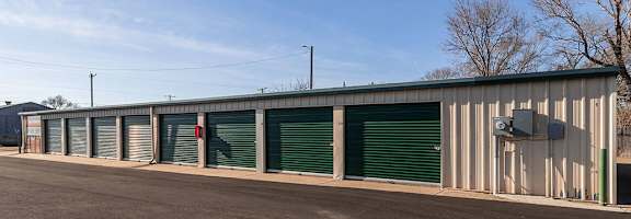 A long building with green doors and a grey roof.