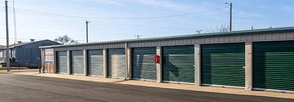A row of storage units with green doors and closed shutters.