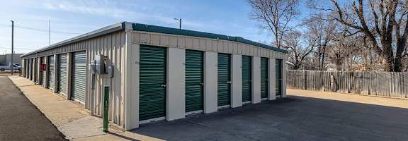 A long building with green doors is surrounded by a fence.