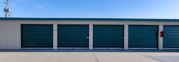 A row of four blue storage doors in front of a grey building.