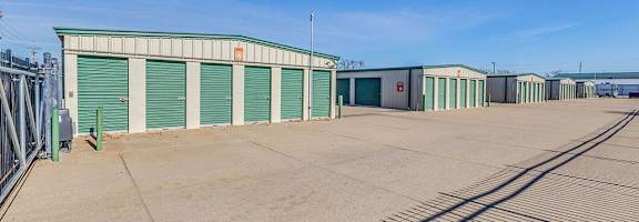 A row of green storage units with closed doors are in a parking lot.