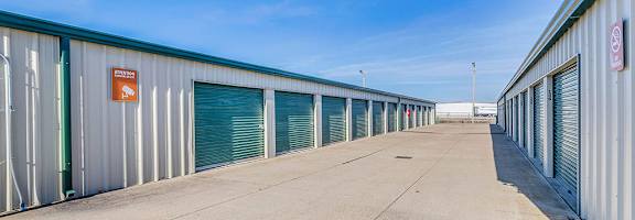 A long row of storage units with green doors and a red sign on the wall.