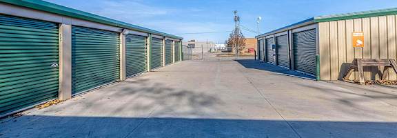 A long row of storage units with green roofs and closed doors.