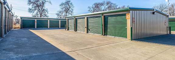 A row of storage units with green doors and a clear blue sky.