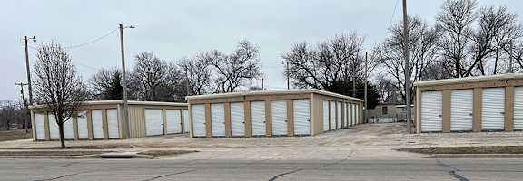 A parking lot with a row of storage units in the background.
