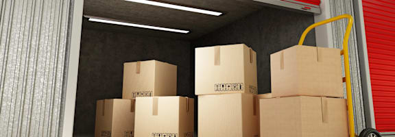 A yellow hand truck is parked in front of a stack of cardboard boxes in a warehouse.