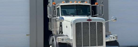 A semi truck is parked in front of a grey building.