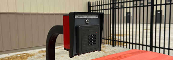 A red car is parked next to a black gate with a parking meter attached to it.
