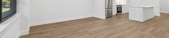 A spacious room with wooden flooring and a kitchen area in the background.