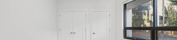A room with two doors and a window overlooking a street.