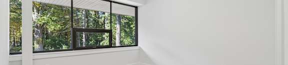 A room with wooden flooring and a window overlooking a forest.